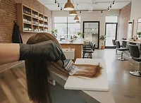 A gloved hand painting lightener onto a section of brown hair on a balayage board