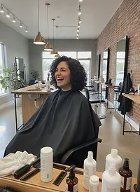 A client laughing in the chair, her dark curly hair cut short and full