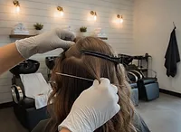 Gloved hands sectioning brown hair at the back of the head for a weft row