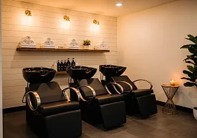 The shampoo area: three black shampoo chairs under shelves of rolled towels