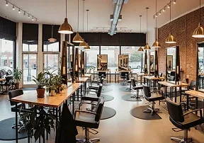 A row of styling stations with wood-framed mirrors and black chairs in a sunlit room
