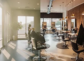 The salon floor on a sunny afternoon: black chairs at wood-framed mirrors, a stylist working at the far station
