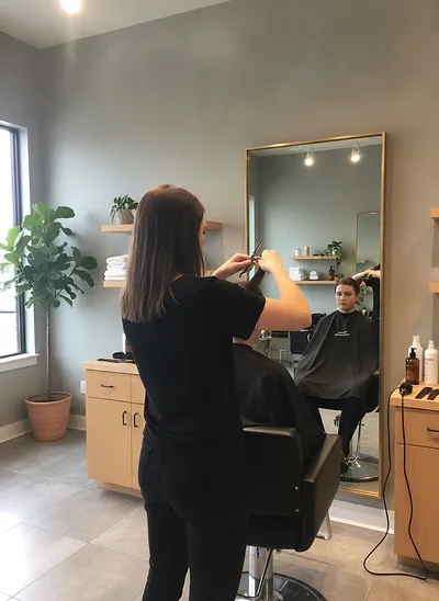 A stylist cutting a client's hair at a mirrored station, seen from behind